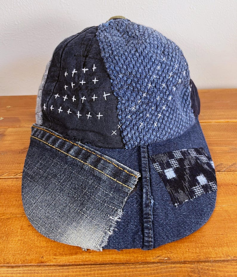May include: A blue denim baseball cap with a patchwork design. The cap is made of different shades of blue denim and features a black and white checkered patch on the side.
