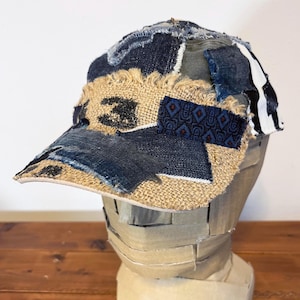 May include: A brown and blue patchwork baseball cap with a frayed brim. The cap is made of different fabrics, including denim, burlap, and a patterned fabric.