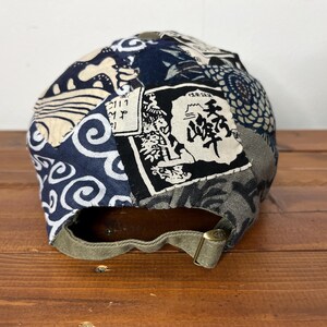 May include: A baseball cap featuring a patchwork design of navy blue, white, and grey fabric panels with various patterns including waves and floral motifs. A rectangular patch with black Japanese kanji text is visible on the back panel.