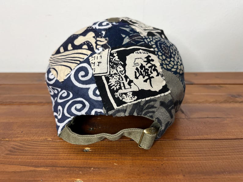 May include: A baseball cap featuring a patchwork design of navy blue, white, and grey fabric panels with various patterns including waves and floral motifs. A rectangular patch with black Japanese kanji text is visible on the back panel.