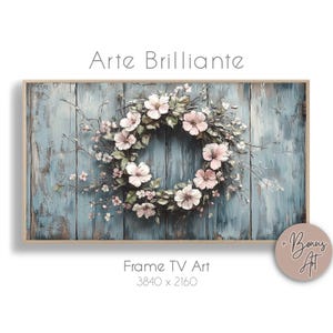 May include: A framed digital art print featuring a floral wreath with pink and white flowers on a weathered blue wooden background. The text "Arte Brillante" is at the top, and "Frame TV Art" with dimensions is at the bottom.
