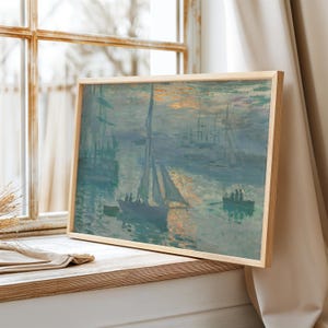 May include: A framed painting of a seascape with a sailboat in the foreground and other boats in the distance. The sky is a pale blue with hints of pink and orange, suggesting a sunrise or sunset. The water is a light blue and green, with reflections of the boats and the sky.