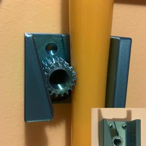 May include: A teal-colored, 3D-printed wall mount with a gear-shaped opening. The mount is designed to hold a cylindrical object, with a yellow cylinder in place. The mount is attached to an orange wall.