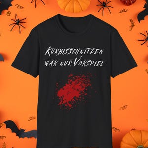 May include: A black short-sleeved t-shirt featuring the white text "KÜRBISSCHNITZEN WAR NUR VORSPIEL" printed on the chest, accompanied by a red graphic resembling a blood splatter located below the text on the front of the garment.