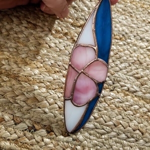 Pode incluir: Um ornamento de vitral oval. Apresenta sec&ccedil;&otilde;es de vidro branco, rosa e azul, contornadas com metal cor de cobre. Uma argola de arame de cobre est&aacute; no topo para pendurar. Mede aproximadamente 15 cm de comprimento.