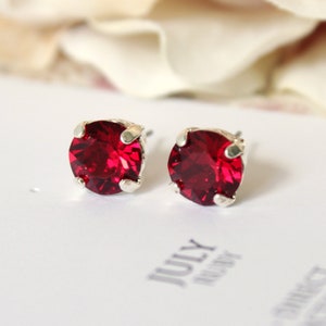 May include: A pair of silver stud earrings with a round, bright red gemstone in the center of each earring.