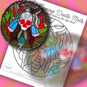 May include: A circular stained glass piece featuring a moth with a skull-shaped body in white, red, and blue, surrounded by green and red flames. Beside it is a paper pattern titled Flaming Death Moth by Sloe-Eyed Solder with an 8-inch diameter.