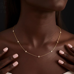 May include: A delicate gold necklace featuring several round, clear gemstones evenly spaced along a fine chain. The necklace is displayed on a person's skin, with the focus on the jewelry's design and sparkle.