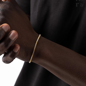 May include: A gold chain bracelet on a person's wrist.