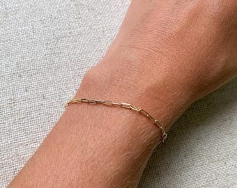 May include: A gold chain bracelet with a delicate, linked design. The bracelet is shown on a person's wrist.