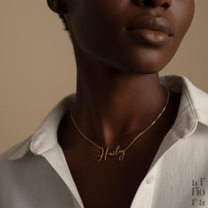 May include: A gold-colored necklace with the name "Hailey" in cursive script. The necklace is worn against a white collared shirt. The image is a close-up shot, focusing on the necklace and the upper chest area.