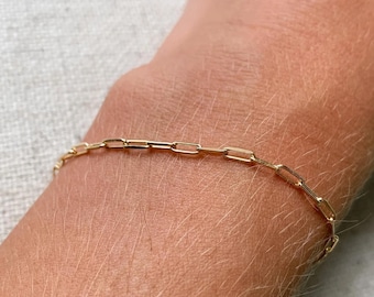 May include: A gold chain bracelet with a delicate, linked design. The bracelet is worn on a person's wrist.