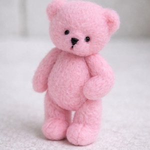 Op de afbeelding: Een kleine, handgemaakte roze teddybeer met zwarte ogen en een zwarte neus. De beer staat rechtop, met zijn armen en benen licht uitgestrekt. Het zachte, pluche speelgoed is een klassiek kinderartikel.