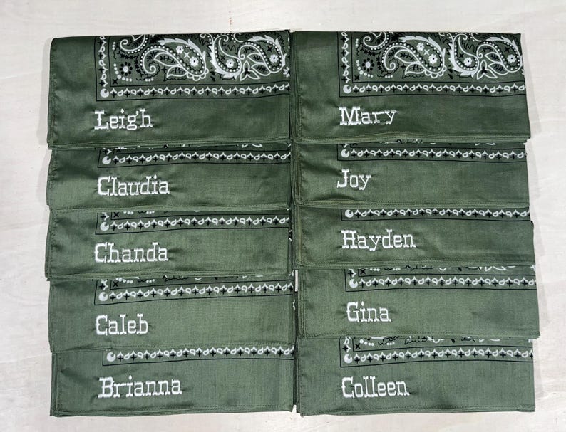 May include: Ten olive green bandanas arranged in two columns, each featuring a white paisley border pattern and a unique name embroidered in white thread. The names include Leigh, Mary, Claudia, Joy, Chanda, Hayden, Caleb, Gina, Brianna, and Colleen.