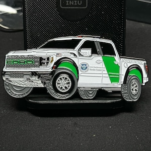 Könnte beinhalten: Eine detaillierte Münze, die einen weißen und grünen Ford-Truck mit dem Text "FORD" auf der Vorderseite zeigt. Die Münze trägt den Text "BORDER PATROL" und das Siegel des US-Zolls und Grenzschutzes. Die Münze hat den Text "RJB2024".