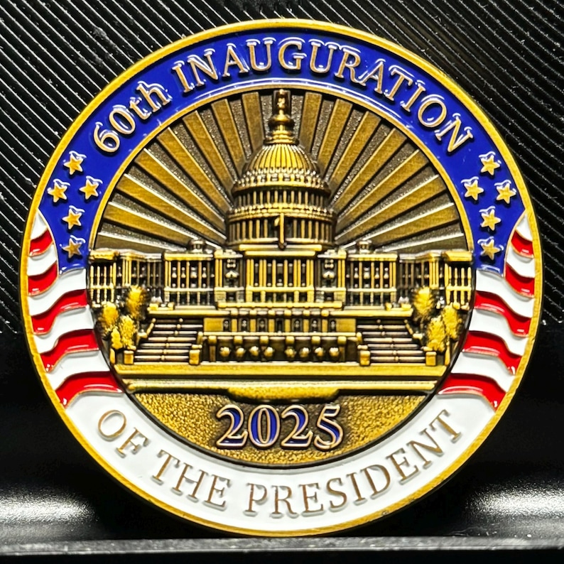 Pu&ograve; includere: Una moneta dorata con una bandiera americana blu e bianca su ogni lato. Al centro della moneta &egrave; raffigurato il Campidoglio degli Stati Uniti con il testo "60th Inauguration of the President 2025".