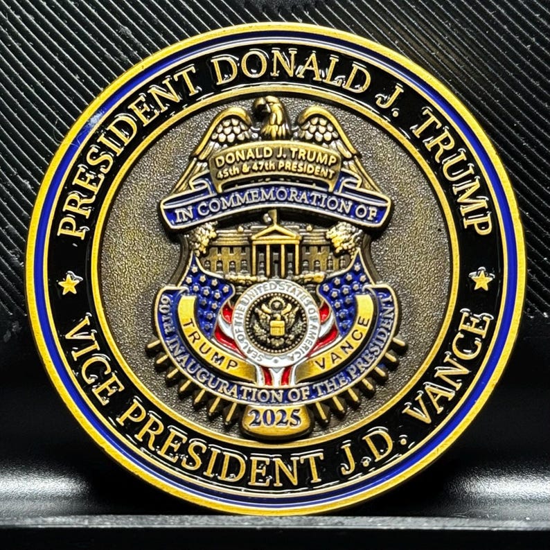 Pu&ograve; includere: Una moneta commemorativa dorata con un anello esterno nero e blu. La moneta presenta un'aquila, la Casa Bianca e il testo "PRESIDENT DONALD J. TRUMP IN COMMEMORATION OF VICE PRESIDENT J.D. VANCE 2025".
