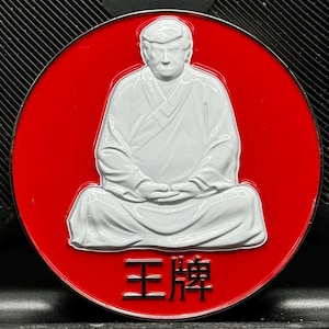 Puede incluir: Una figura blanca de una persona sentada en una postura meditativa sobre un fondo rojo. La figura lleva una túnica blanca y tiene una barba blanca. El texto "王牌" está escrito en negro debajo de la figura.