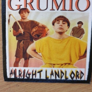 May include: A black and white patch with the text "GRUMIO ALLRIGHT LANDLORD" in a yellow and orange font. The patch features a photo of three men in a vintage style.
