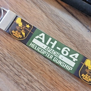 May include: A green, black and yellow key chain with the text "AH-64 APACHE HELICOPTER GUNSHIP" and a graphic of a helicopter with the text "AH-64 APACHE GUNSHIP".