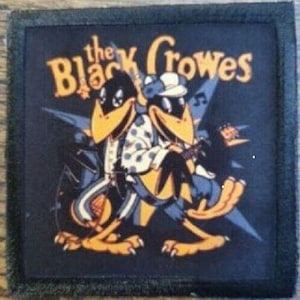May include: Square patch with the text "the Black Crowes" in yellow and a cartoon illustration of two crows playing musical instruments. The crows are in black, yellow, and blue, with a starburst design in the background.