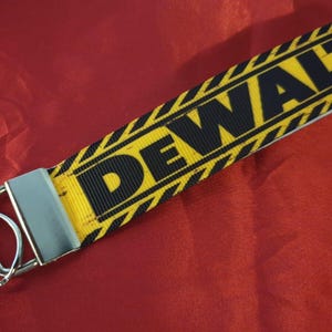 May include: A yellow and black key chain with the word "DEWALT" printed on it. The key chain has a silver metal ring.