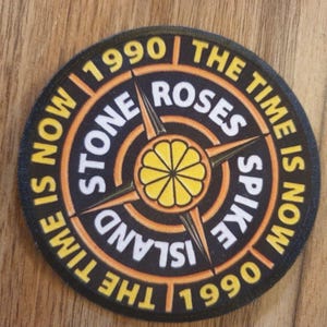 May include: A black and orange circular patch with the text "The Time Is Now" and "Stone Roses" in a compass design. The text "Spike Island" is in the centre of the compass. The years "1990" and "1991" are on either side of the compass.