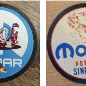May include: Two round Mopar car badges. The first badge is blue with a black border and features a cartoon image of a coyote and a roadrunner sitting on toilets. The second badge is white with a black border and features a blue Mopar logo with the text "Powered Since 1937".