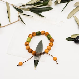 May include: A wooden bracelet with brown and green beads, tied with a brown cord. The bracelet is on a white surface with a green leaf.