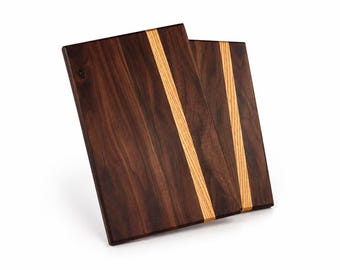 May include: Two rectangular wooden cutting boards featuring a dark brown walnut wood grain surface with a single vertical inlay of light tan wood running off-center across the length of each board, showcasing a smooth, flat, and polished finish.