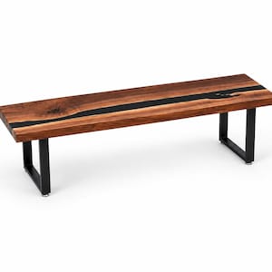 May include: A rectangular bench featuring a natural live-edge wood slab top with a prominent dark brown grain and a central black resin inlay. The bench is supported by two black metal U-shaped legs, providing a stable base for the wooden seat.