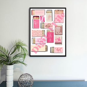 May include: A framed collage of 16 matchboxes with pink and white designs. The matchboxes feature various illustrations, including cowboy boots, hats, and a cocktail glass. The text "Yes, that's how we roll" is visible on one of the matchboxes.