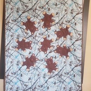 K&ouml;nnte beinhalten: Eine blaue und braune Tarnstoffdecke mit acht braunen Teddyb&auml;r-Applikationen. Die B&auml;ren sind alle in die gleiche Richtung ausgerichtet und haben ein einfaches gesticktes Gesicht.