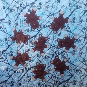 K&ouml;nnte beinhalten: Ein blauer und brauner Tarnstoff mit acht braunen Teddyb&auml;ren, die darauf gen&auml;ht sind. Die B&auml;ren sind alle in die gleiche Richtung gedreht und haben die Augen geschlossen.