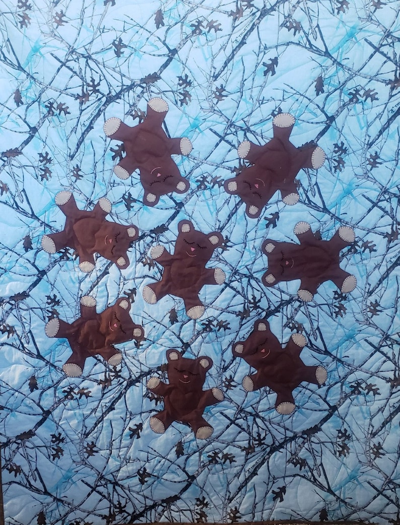 K&ouml;nnte beinhalten: Ein blauer und brauner Tarnstoff mit acht braunen Teddyb&auml;ren, die darauf gen&auml;ht sind. Die B&auml;ren sind alle in die gleiche Richtung gedreht und haben die Augen geschlossen.