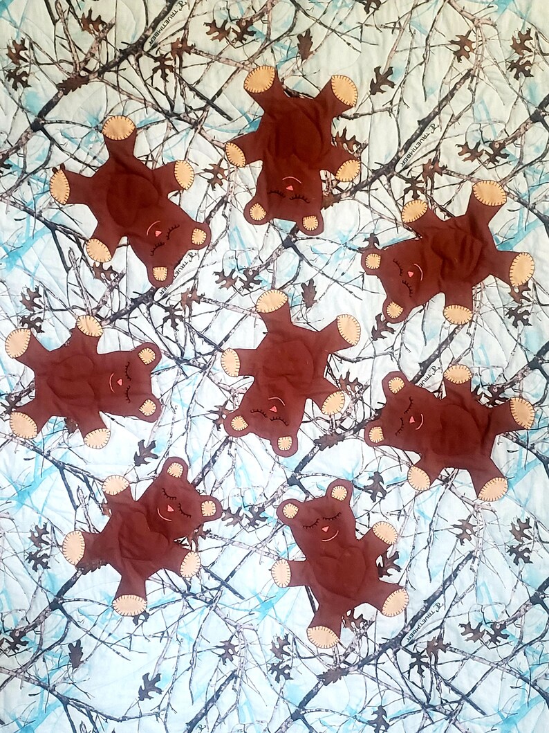 K&ouml;nnte beinhalten: Eine Steppdecke mit einem Tarnmuster, auf der braune Teddyb&auml;ren mit geschlossenen Augen zu sehen sind. Die B&auml;ren sind in verschiedenen Positionen &uuml;ber die Steppdecke verteilt.