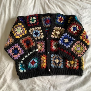 May include: A black, button-up crochet cardigan featuring colorful square patterns. The squares are in various colors, including red, blue, yellow, and green. The cardigan has long sleeves and a classic, comfortable fit. This handmade garment is perfect for adding a unique touch to any outfit.