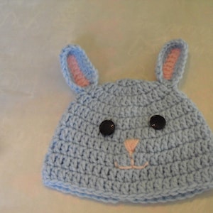 May include: A light blue crocheted bunny hat with pink ears and black button eyes.