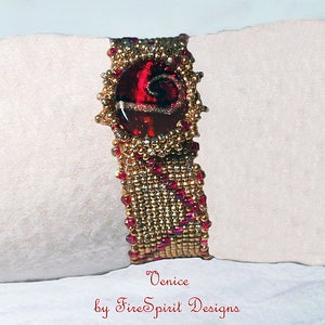 Pode incluir: Um bracelete de contas douradas e vermelhas com uma conta central de vidro vermelho. A conta central tem um design em espiral e um detalhe de brilho dourado. O bracelete &eacute; etiquetado "Venice by Fire Spirit Designs".