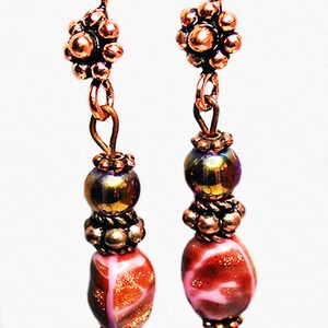 May include: Copper earrings with pink and gold glass beads, copper flower accents, and a copper wire design. The earrings are labeled "Elise by Fire Spirit Designs".