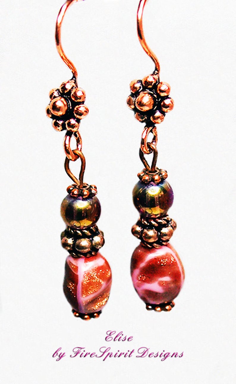 May include: Copper earrings with pink and gold glass beads, copper flower accents, and a copper wire design. The earrings are labeled "Elise by Fire Spirit Designs".