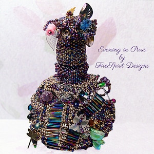 May include: A beaded glass bottle with a purple, gold, and iridescent finish. The bottle is decorated with beads, crystals, and metal accents. The bottle is topped with a beaded cap and a metal leaf. The text "Evening in Paris by Fire Spirit Designs" is visible in the image.