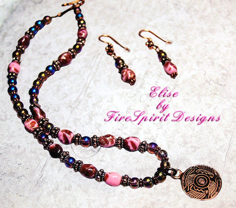 May include: A pink and brown glass bead necklace with a copper pendant featuring a floral design. The necklace is paired with matching earrings. The text "Elise by Fire Spirit Designs" is visible in the image.
