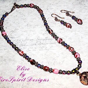 May include: A pink and brown necklace with a copper pendant and matching earrings. The necklace is made of small beads and the pendant is a round, ornate design. The earrings are simple and dangle from copper hooks.