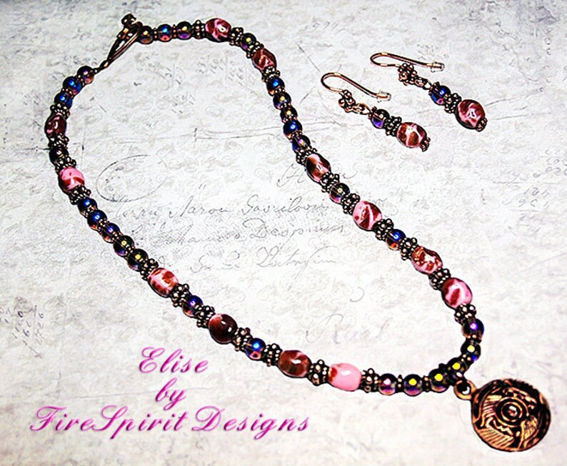 May include: A pink and brown necklace with a copper pendant and matching earrings. The necklace is made of small beads and the pendant is a round, ornate design. The earrings are simple and dangle from copper hooks.