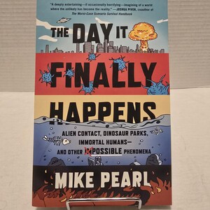 May include: Book cover with a red, white, and blue illustration of a city with a mushroom cloud in the sky. The title is "The Day It Finally Happens" and the subtitle is "Alien Contact, Dinosaur Parks, Immortal Humans- And Other Impossible Phenomena". The author is Mike Pearl.