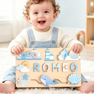 May include: A rectangular wooden puzzle board featuring the name ROMEO in light blue letters, surrounded by nautical-themed wooden shapes including a lighthouse, a whale, seashells, a sun, clouds, and a ship with rotating blue gears.