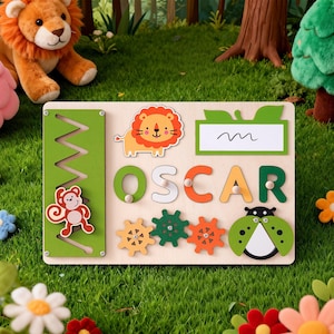 Può includere: Tavola puzzle educativa in legno con il nome "OSCAR" scritto in lettere colorate. Presenta un leone, una scimmia, una coccinella e ingranaggi. Include una pista a zig-zag verde e un'etichetta vuota. La tavola è ambientata su uno sfondo di erba e fiori.