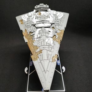 May include: A detailed model of a Star Destroyer starship, in grey and gold. The triangular model has intricate detailing and is mounted on a black base. A collectible item.