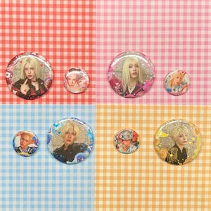 May include: A collection of six round pinback buttons featuring portraits of a person with blonde hair. The buttons vary in size and have glitter and heart accents. The background is a mix of pink, blue, and orange gingham.